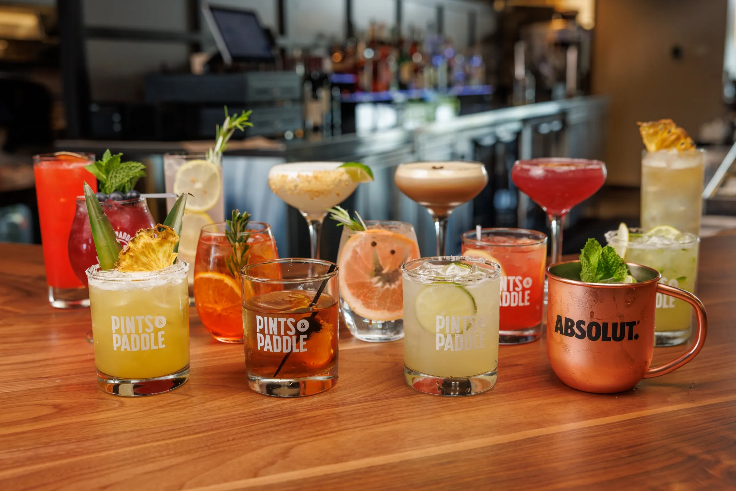 The full cocktail lineup in branded glassware along the walnut bar