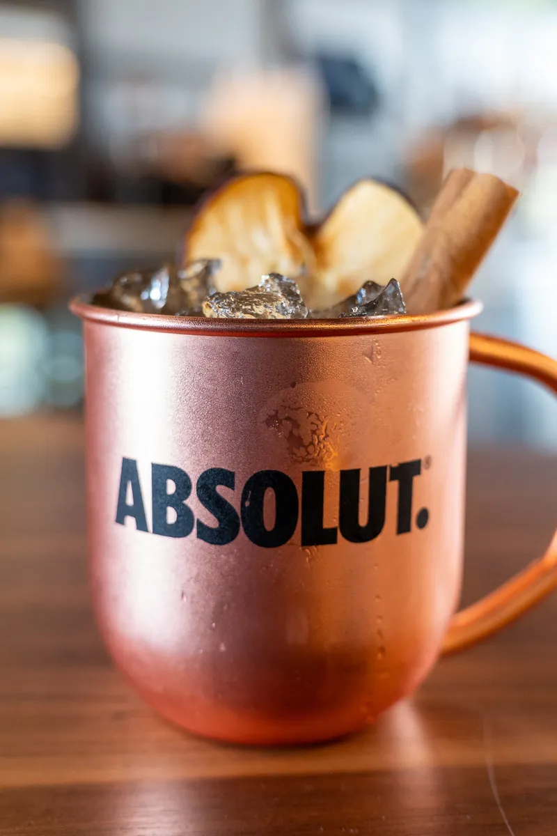 An Autumn Mule in a copper Absolut mug, topped with ice, dried apple slices and a cinnamon stick.