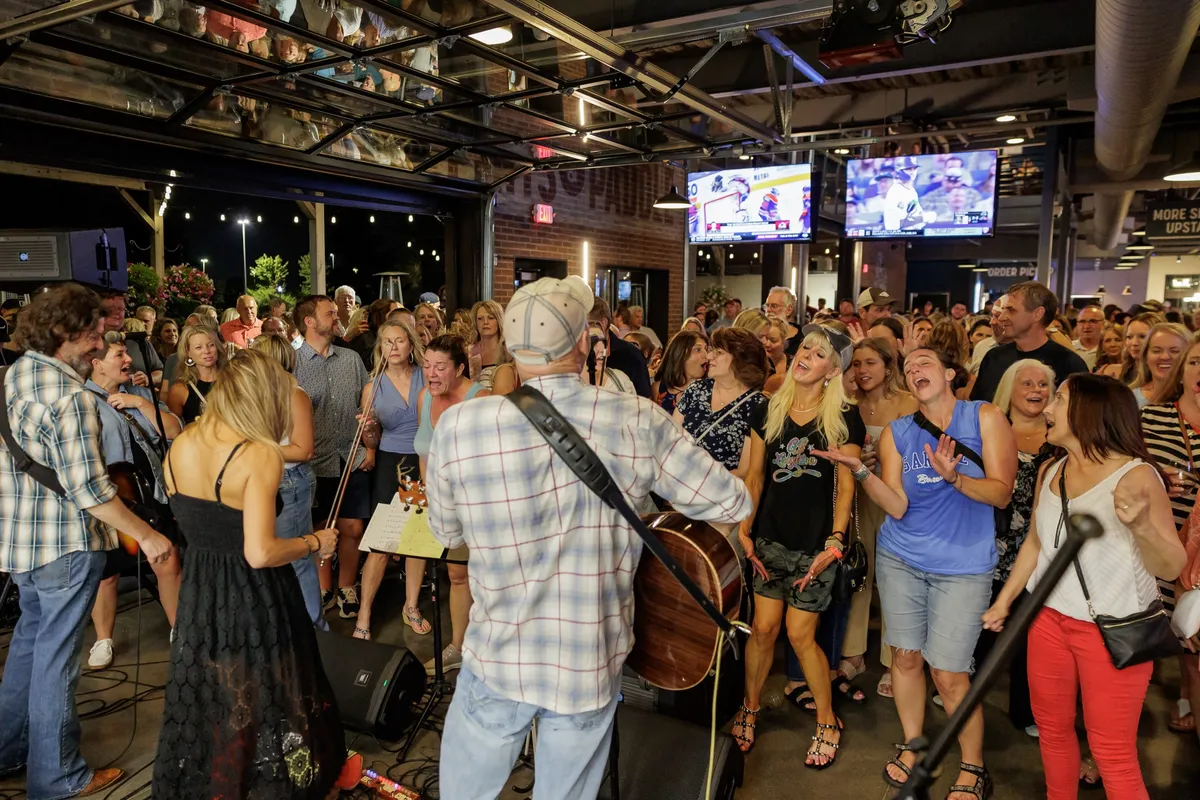 A band plays to a packed, singing crowd by the open garage doors at dusk