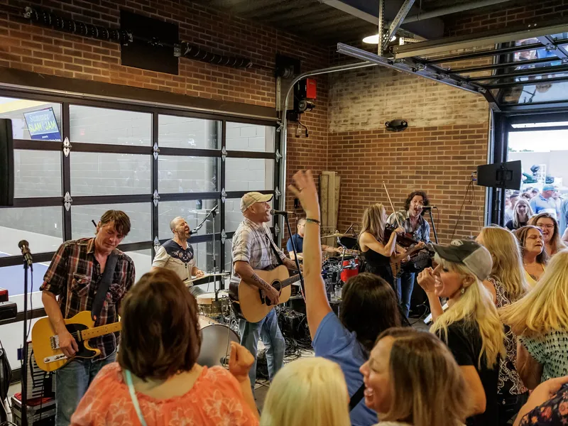 A band plays by the open garage doors while the crowd dances with arms raised
