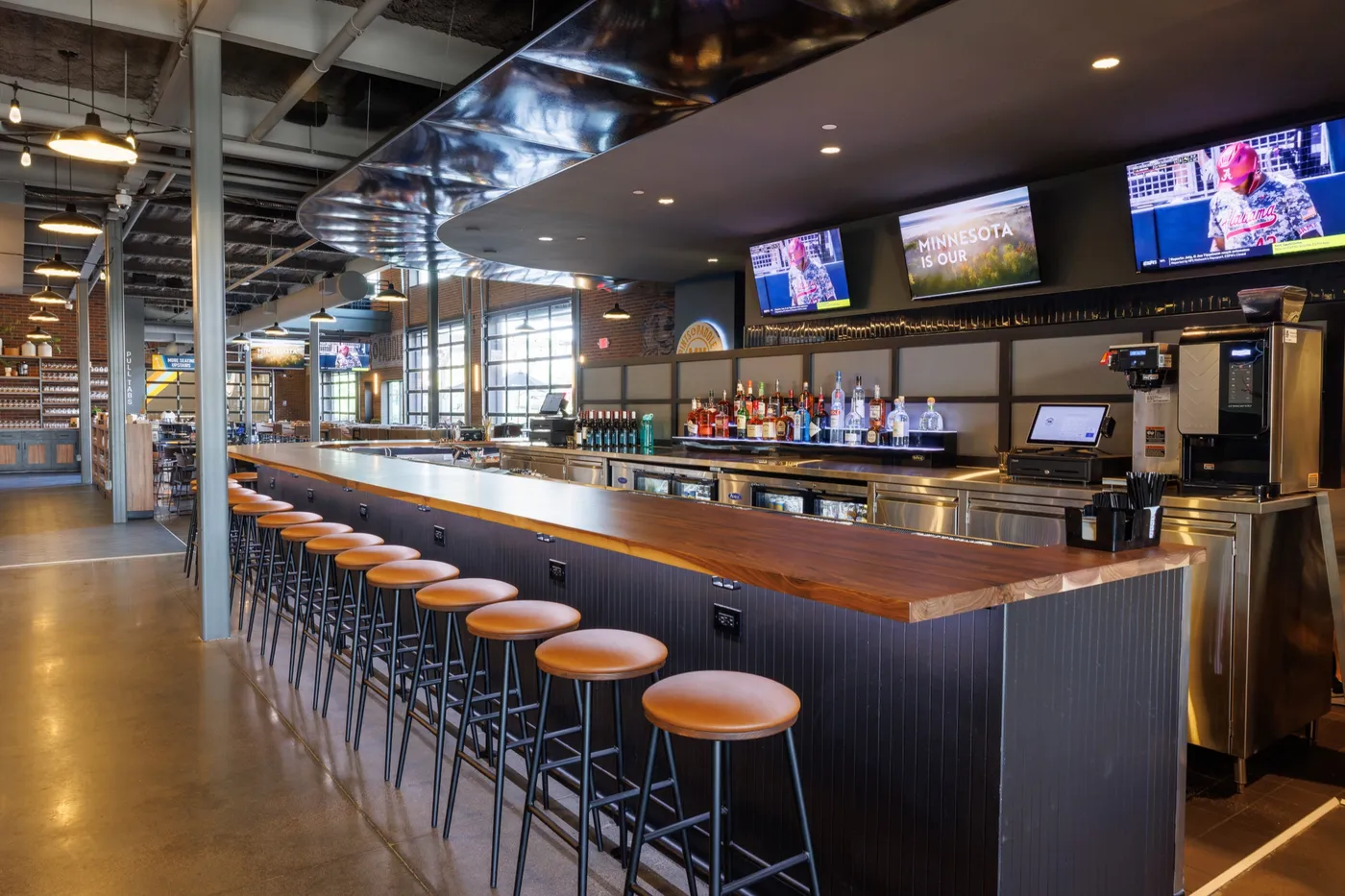 The long walnut bar with a row of leather stools, the lit back bar and the taproom beyond