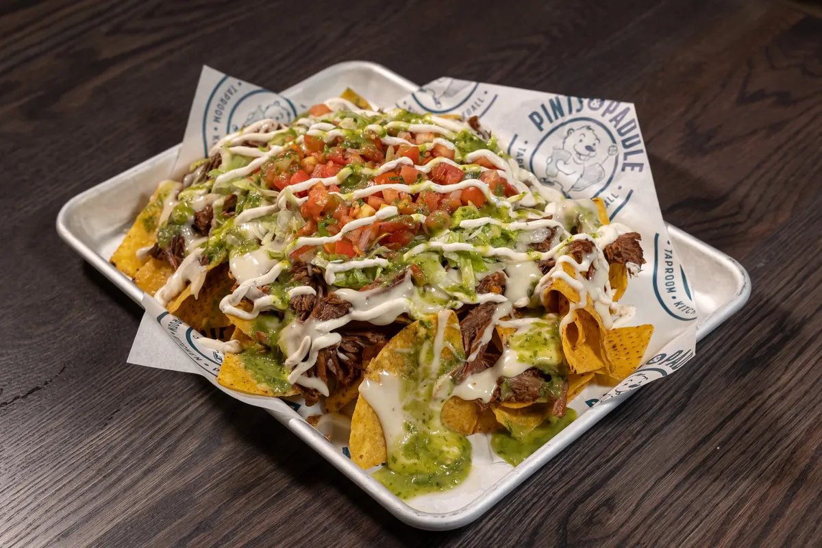 A tray of barbacoa nachos with queso, crema, pico de gallo and salsa verde on branded paper