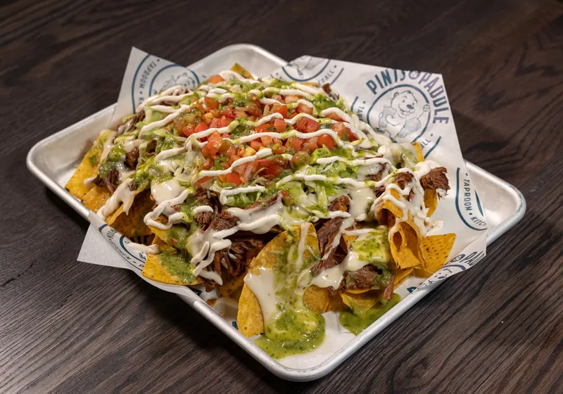 A tray of barbacoa nachos with queso, crema, pico de gallo and salsa verde on branded paper