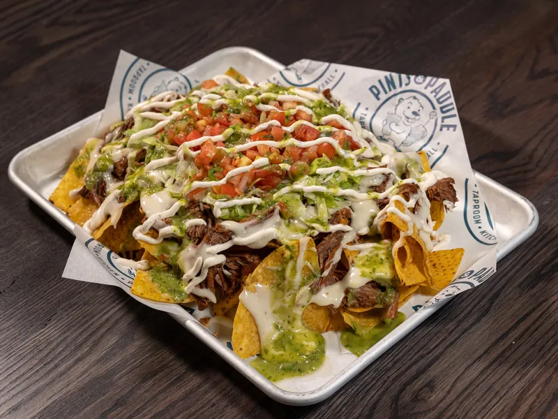 A tray of barbacoa nachos with queso, crema, pico de gallo and salsa verde on branded paper