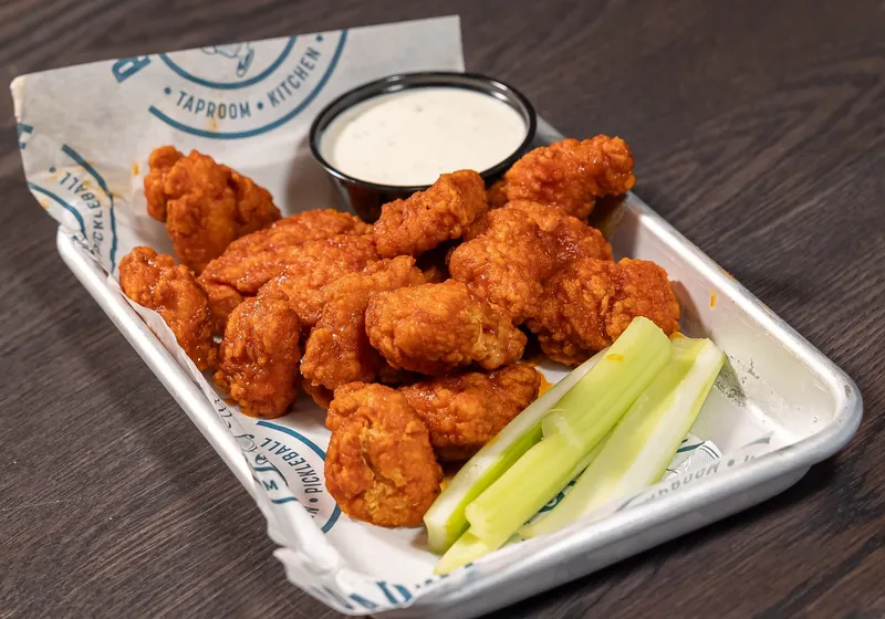 Boneless buffalo wings in a metal tray with a cup of ranch and celery sticks