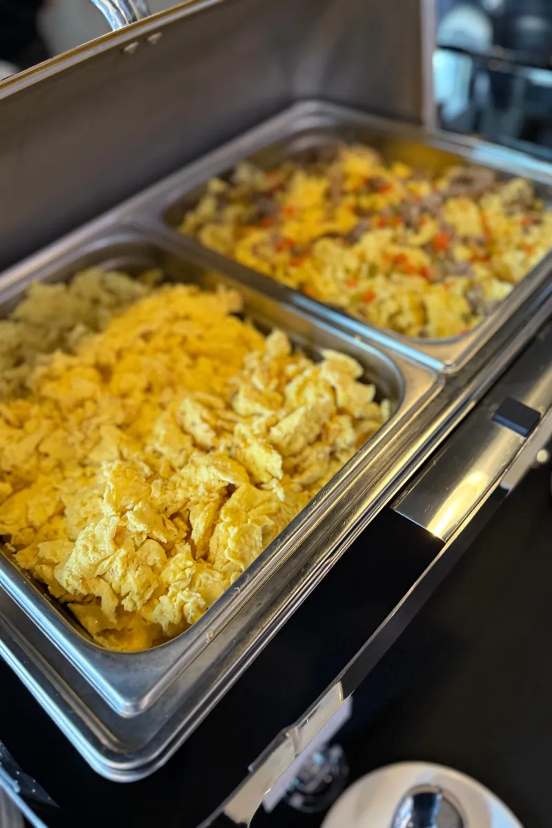 A chafer with two pans of scrambled eggs, one plain and one with sausage and peppers, on a breakfast buffet