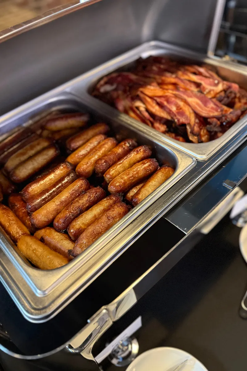 A chafer with a pan of breakfast sausage links and a pan of bacon on a breakfast buffet