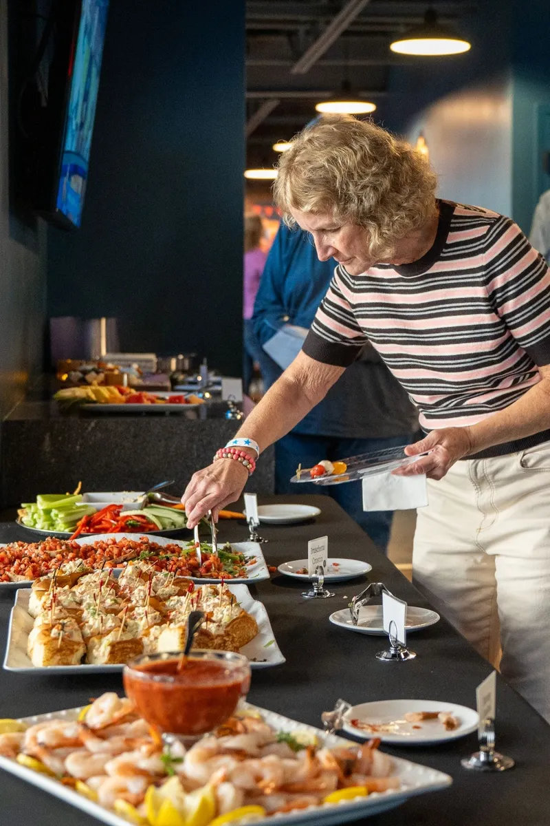 A guest serving herself bruschetta crostini from a catered buffet of shrimp, lobster rolls and crudité on the mezzanine