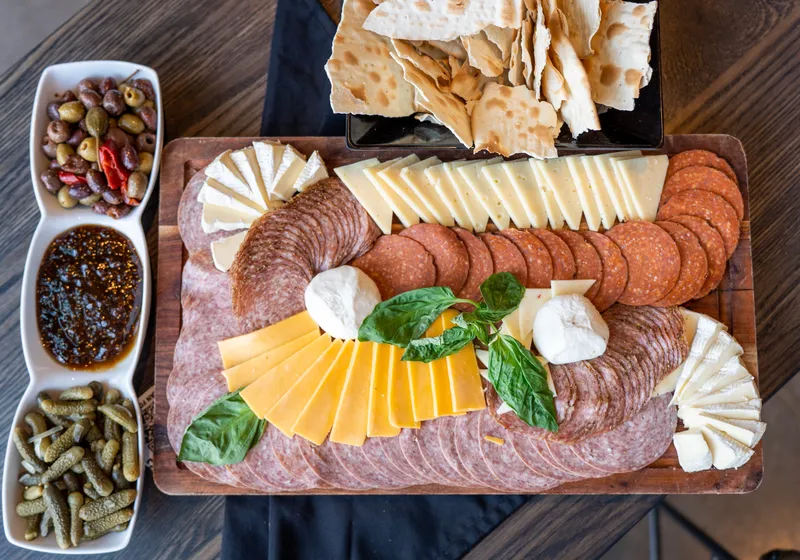 A charcuterie board with salami, capicola, brie, burrata and basil beside olives, fig jam and lavash crackers