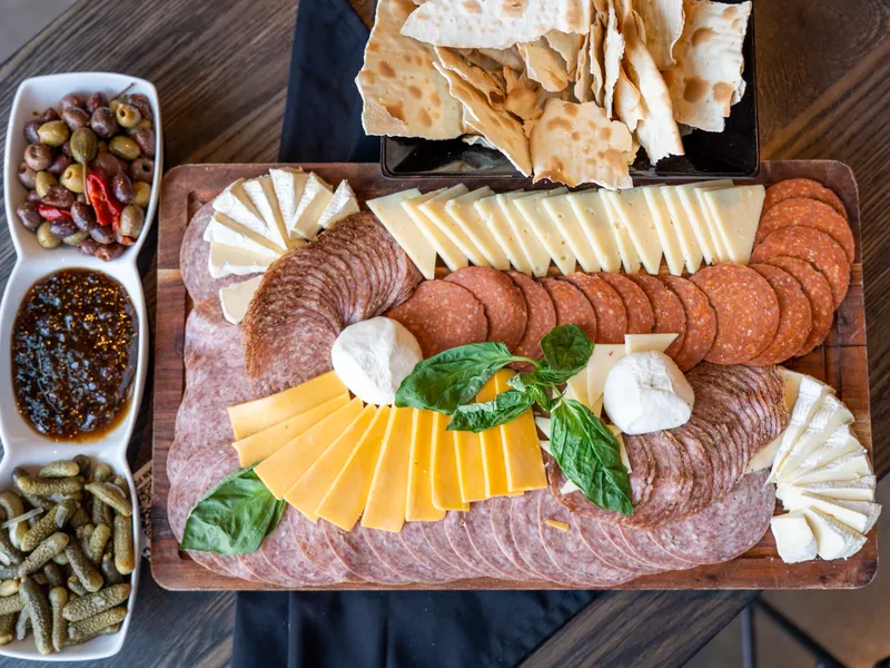 A charcuterie board with salami, cheeses, brie and burrata beside olives, fig jam and crackers