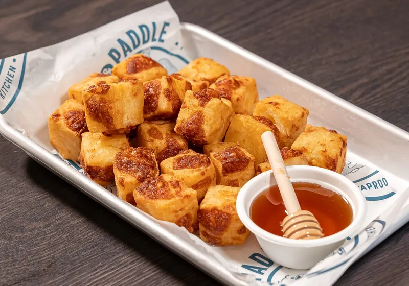 Fried cheese curds with a ramekin of hot honey and a wooden honey dipper on branded parchment