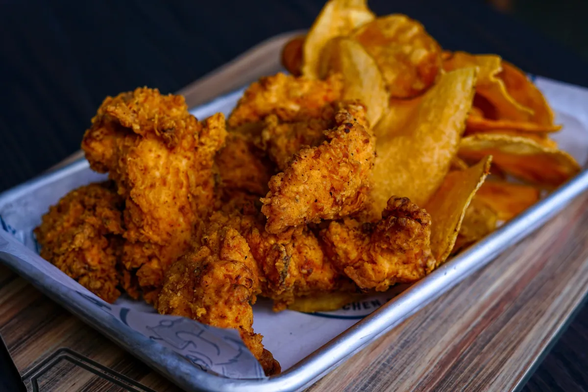 Crispy chicken strips with house kettle chips on a metal tray