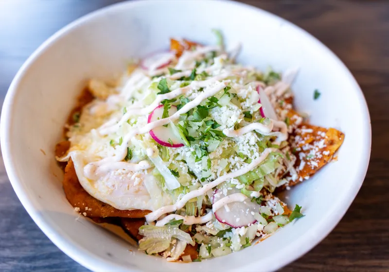 A bowl of chilaquiles topped with a fried egg, shredded lettuce, queso fresco, radish, cilantro and sour cream