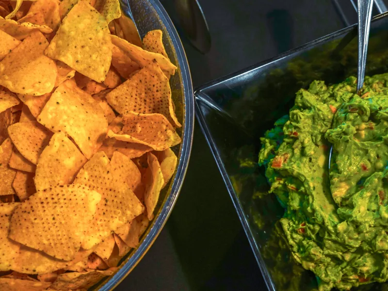A bowl of house tortilla chips beside a bowl of fresh guacamole with a serving spoon