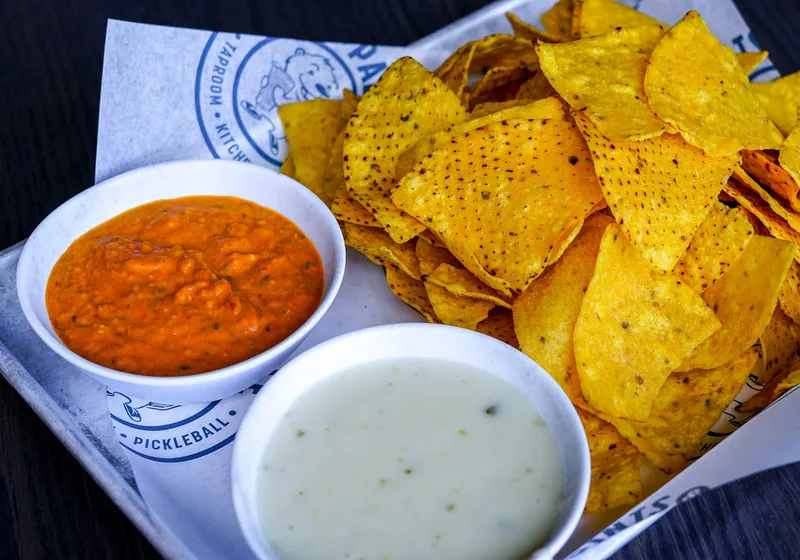 A tray of fresh tortilla chips with a bowl of red salsa and a bowl of queso blanco on branded paper