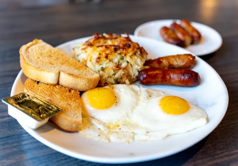 A classic breakfast plate with two sunny-side-up eggs, cheesy hash browns, sausage links and toast