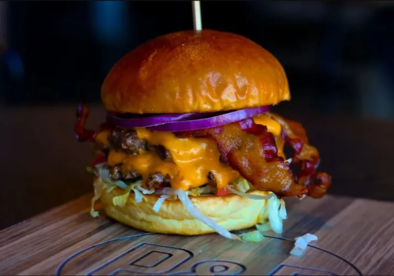 The Classic Bacon and Cheese burger with bacon, melted cheese, red onion and shredded lettuce on a branded wooden board