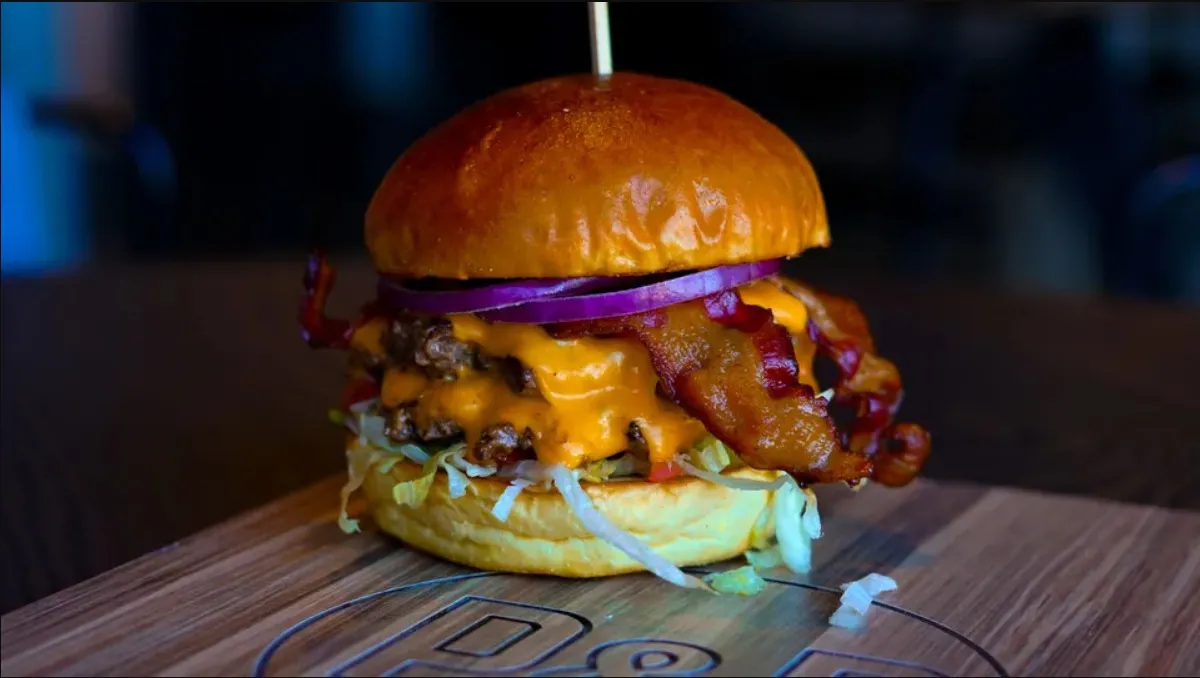 The Classic Bacon and Cheese burger with bacon, melted cheese, red onion and shredded lettuce on a branded wooden board