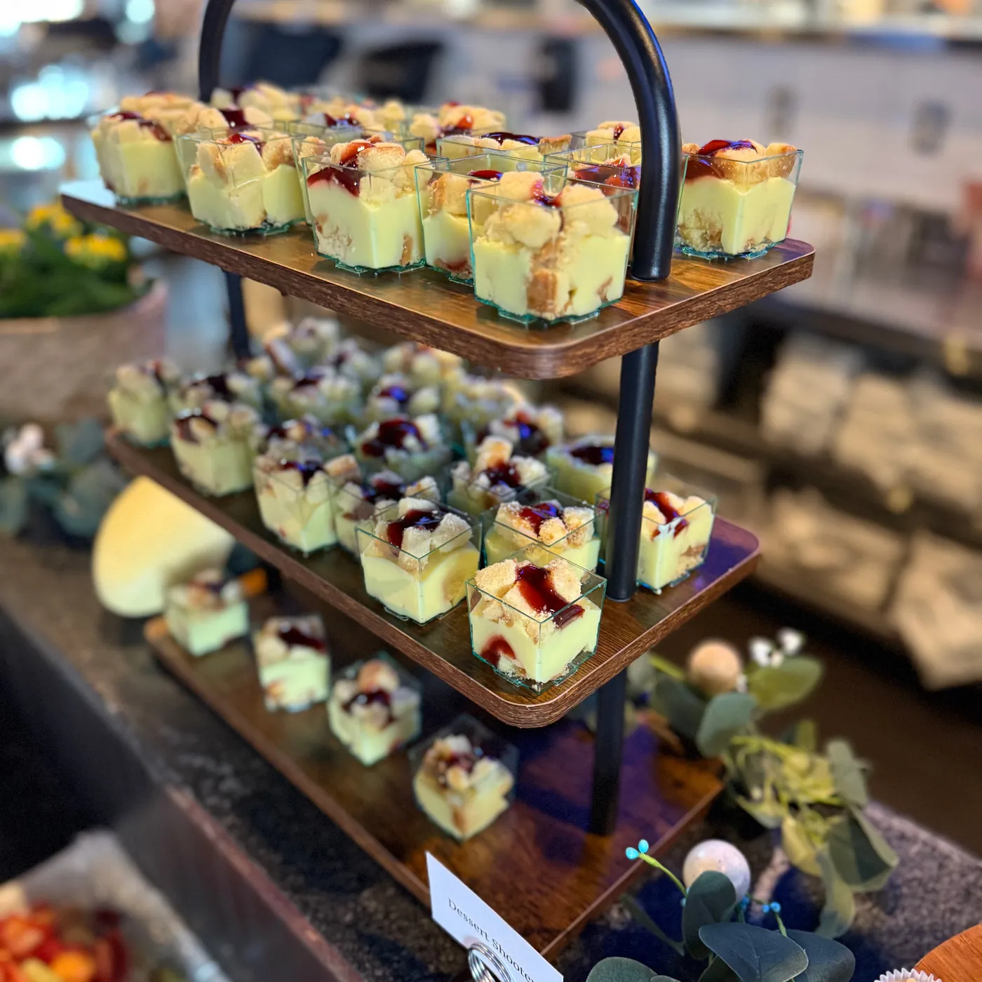 A three-tier stand of layered dessert cups topped with berry sauce on the buffet counter, a fruit tray in front