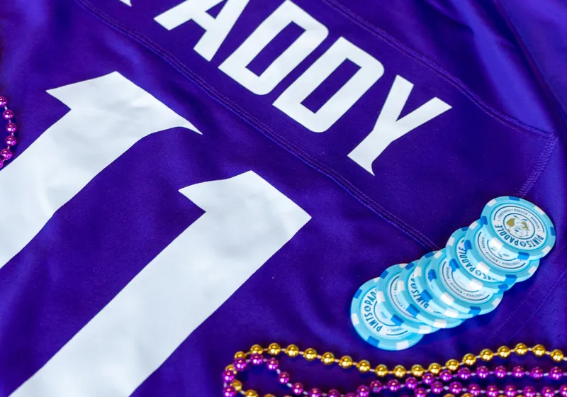 A fan of light-blue Pints & Paddle drink chips on a purple Paddy 11 jersey with purple-and-gold beads