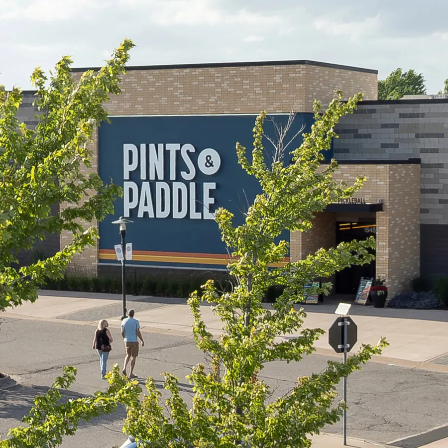 Elevated view of the building front with the big navy PINTS & PADDLE sign on tan brick and the covered PICKLEBALL entrance
