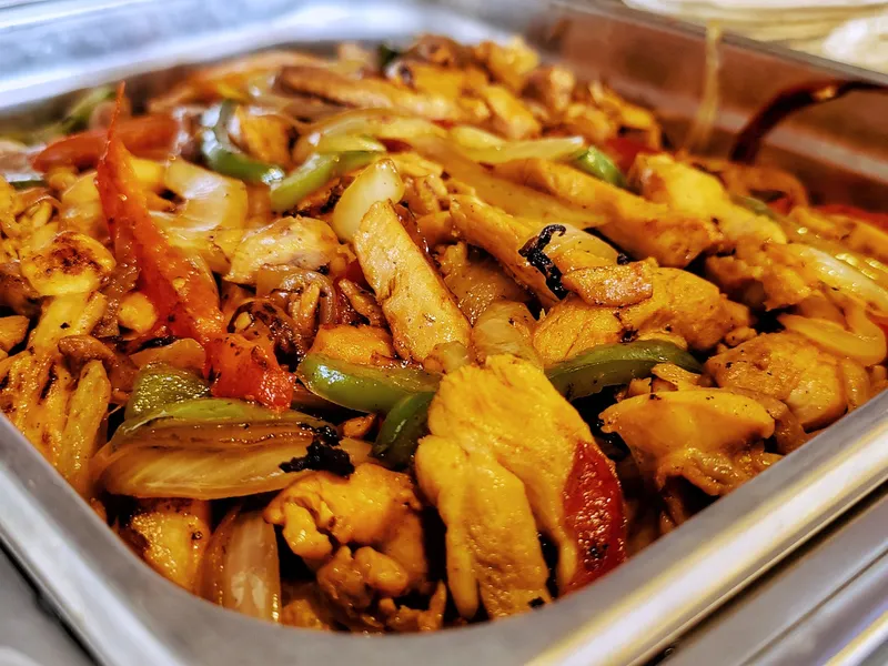 A stainless chafer pan of fajita chicken with peppers and onions, warm flour tortillas behind
