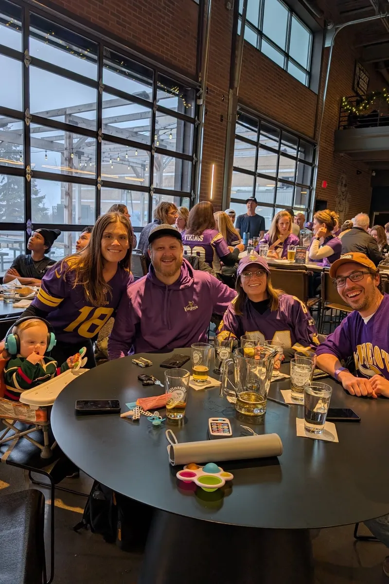 A family in purple around a round table by the garage doors, a toddler in a high chair at the end