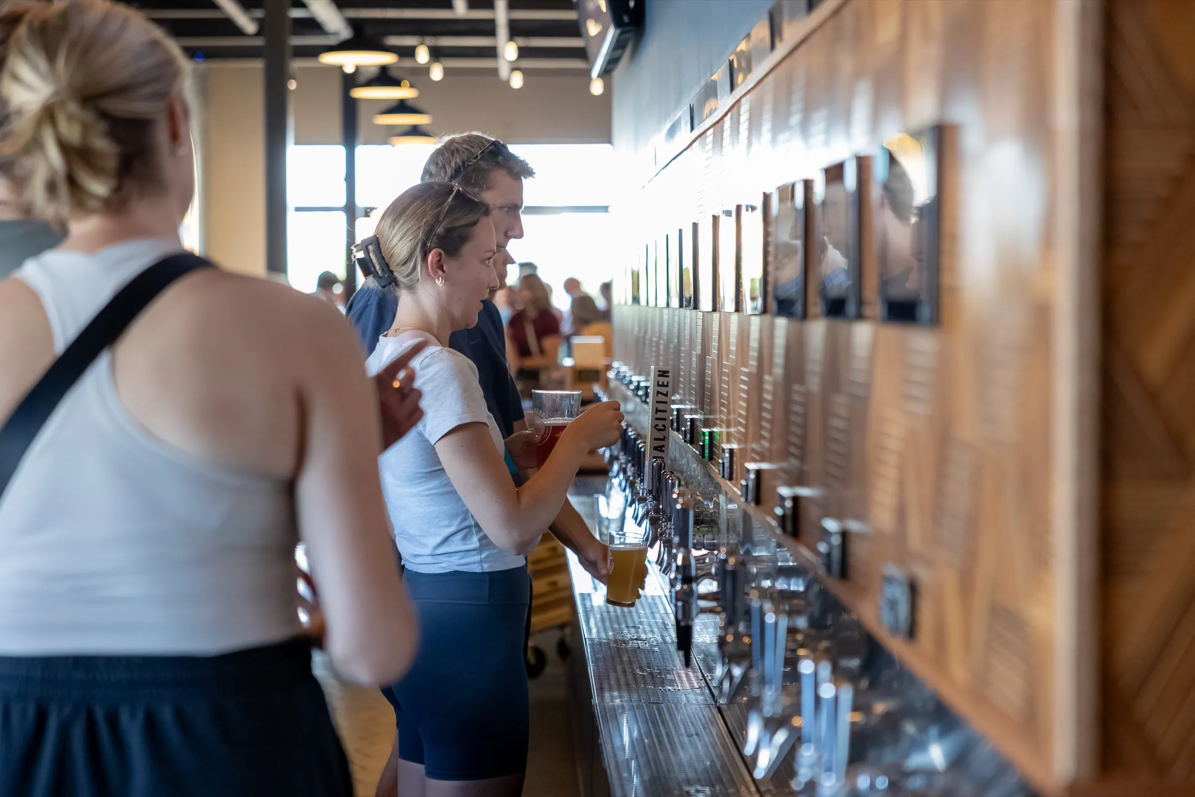 Two guests pouring their own beers at the self-serve tap wall