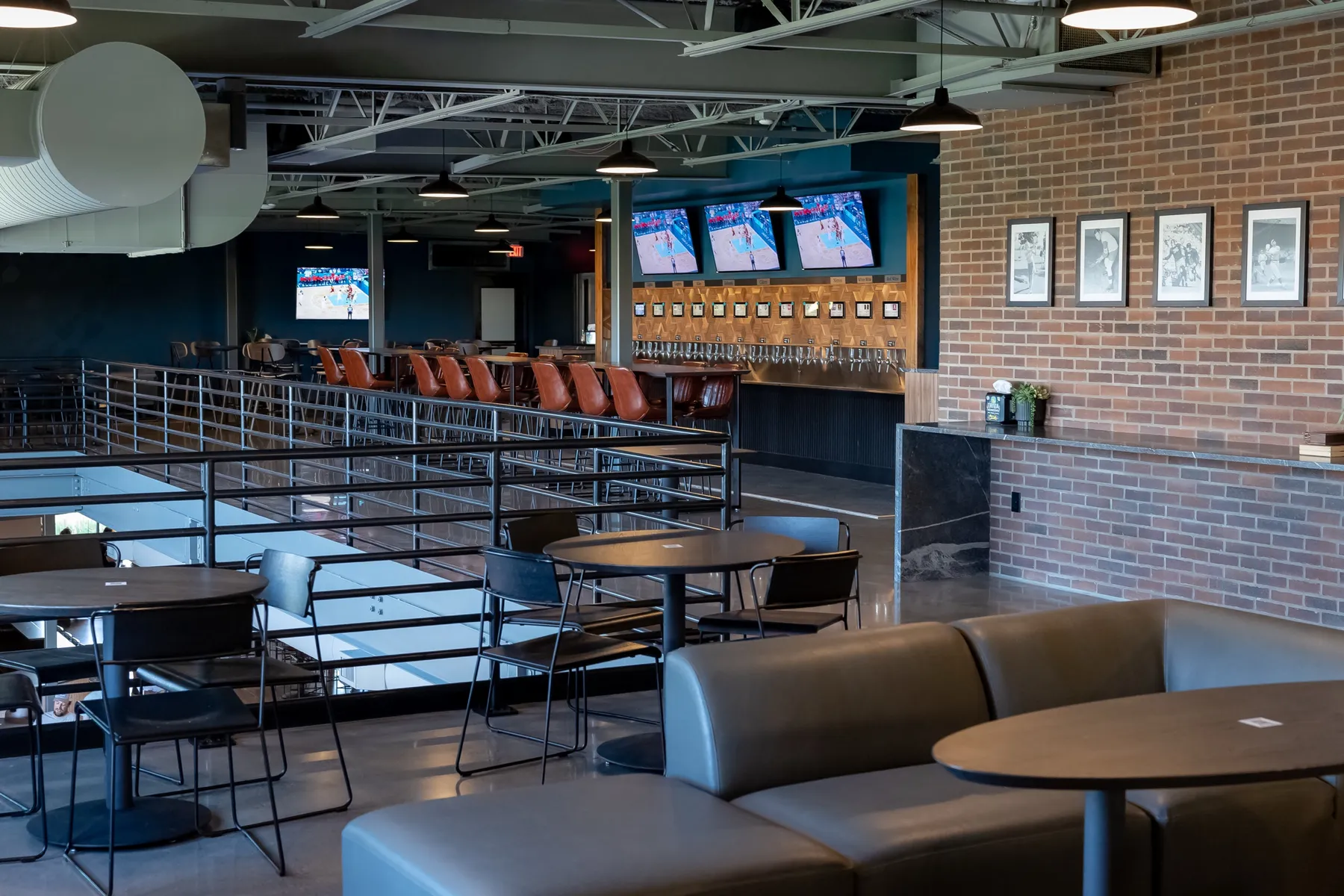 The full mezzanine with round tables, a leather banquette, the self-serve tap wall and TVs