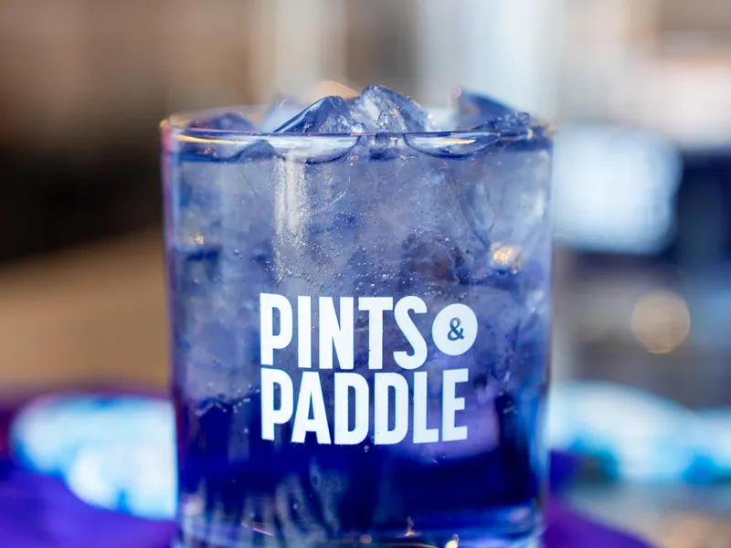 A purple Grape Ape cocktail over ice in a Pints & Paddle rocks glass, set on a purple jersey