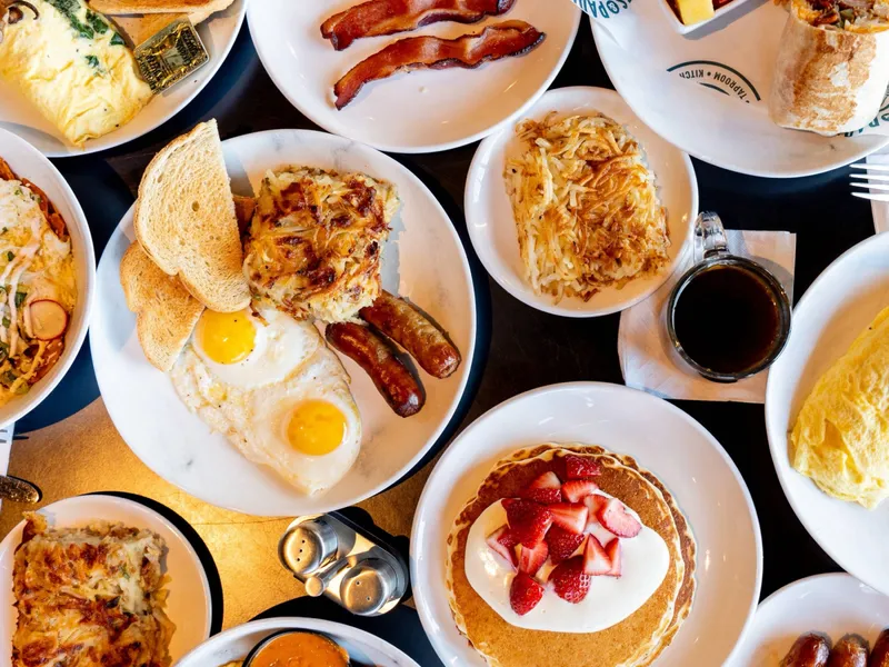 Overhead view of the full weekend breakfast spread: pancakes, eggs, bacon, an omelette, a breakfast wrap and coffee