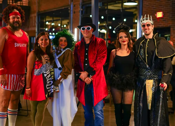 Six guests in Halloween costumes lined up in the taproom, from a headband and striped shorts to Willy Wonka, an Oompa Loompa, Maleficent and a crowned king