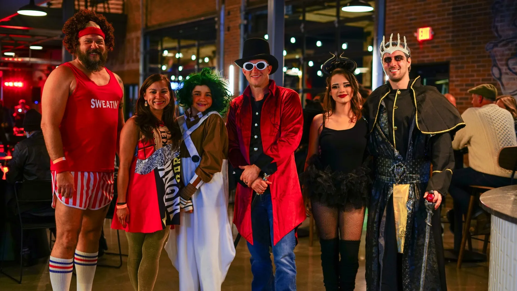Six guests in Halloween costumes lined up in the taproom, from a headband and striped shorts to Willy Wonka, an Oompa Loompa, Maleficent and a crowned king