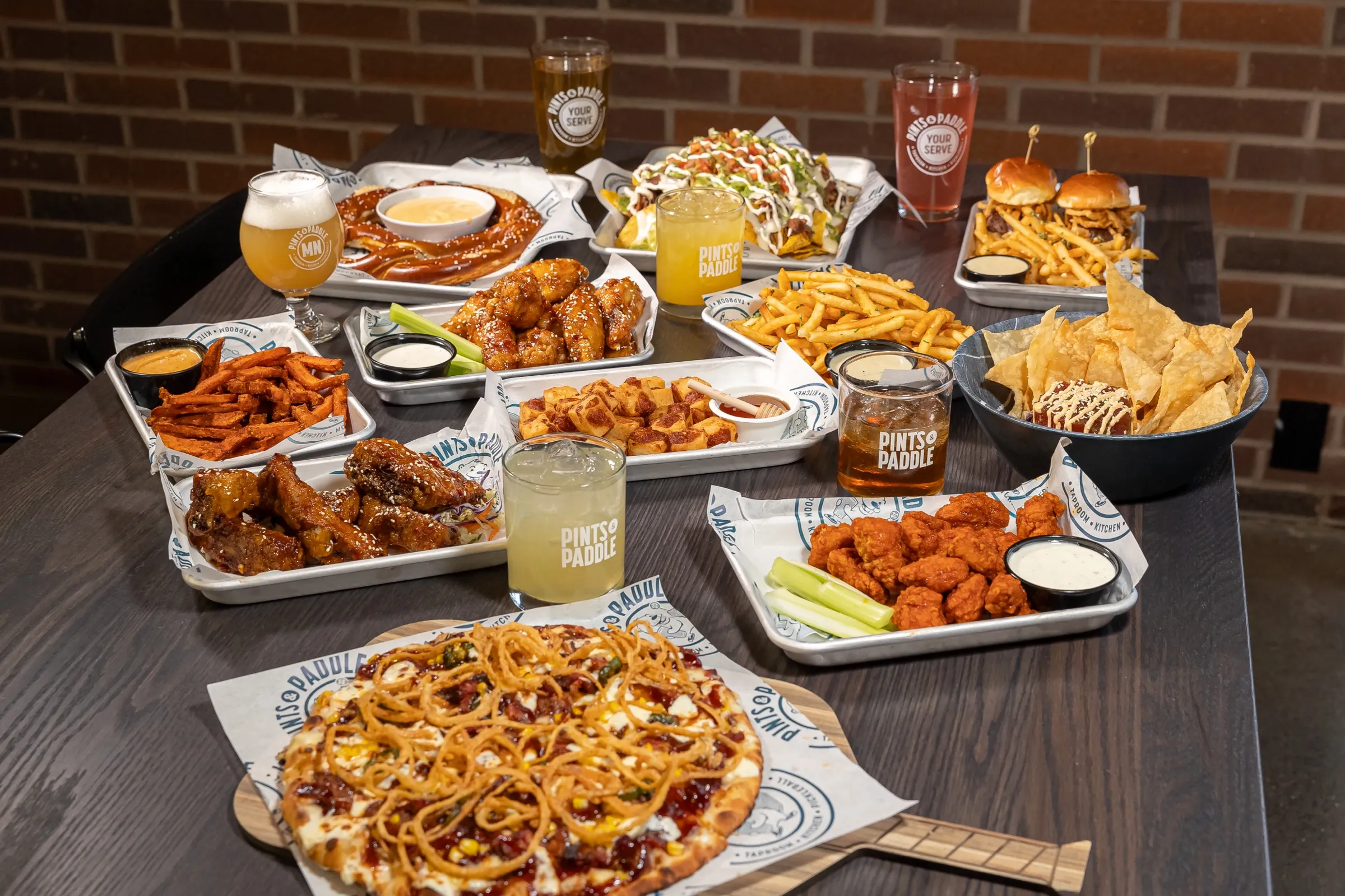 A full spread of shareables from above: flatbread, pretzel with beer cheese, nachos, sliders with fries, wings, cheese curds and drinks