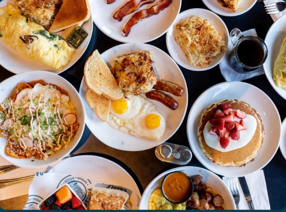 A table of breakfast plates from above: eggs, bacon, hash browns, pancakes with strawberries, chilaquiles and toast