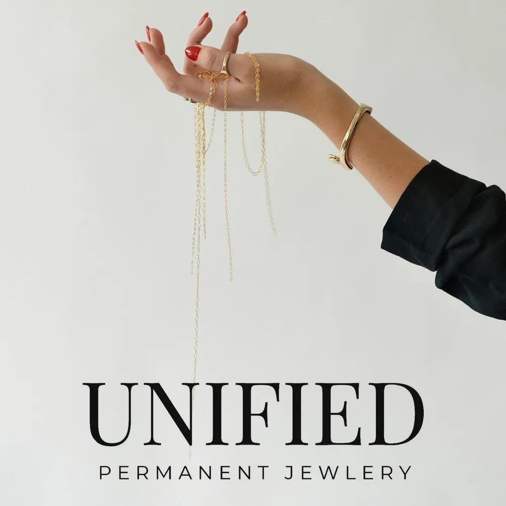 A hand dangling fine gold chains, a gold bracelet on the wrist, with the Unified Permanent Jewelry logo