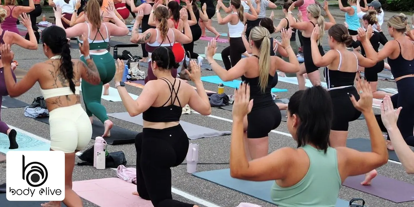 A Body Alive Pilates class on mats in a parking lot, a crowd of women in a lunge with arms raised