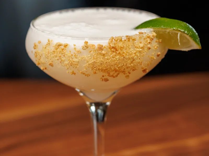 A key lime pie martini in a coupe with a graham-cracker crumb rim and a lime wedge