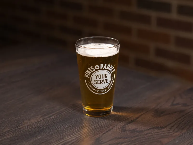 A pint of light golden lager with a foam head in a Pints & Paddle glass