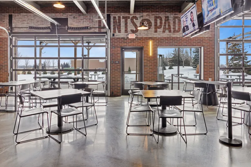 Wide view of the main-level floor with dining tables in front of the glass overhead doors and brick wall