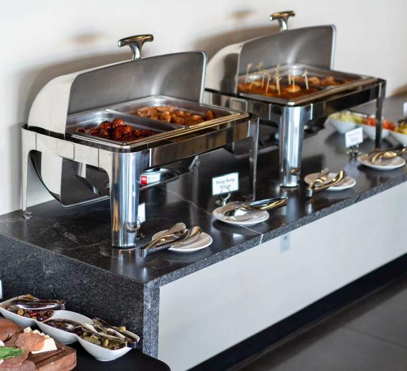 Two open chafers of wings and sliders with serving tongs and name cards on the main-level granite buffet counter
