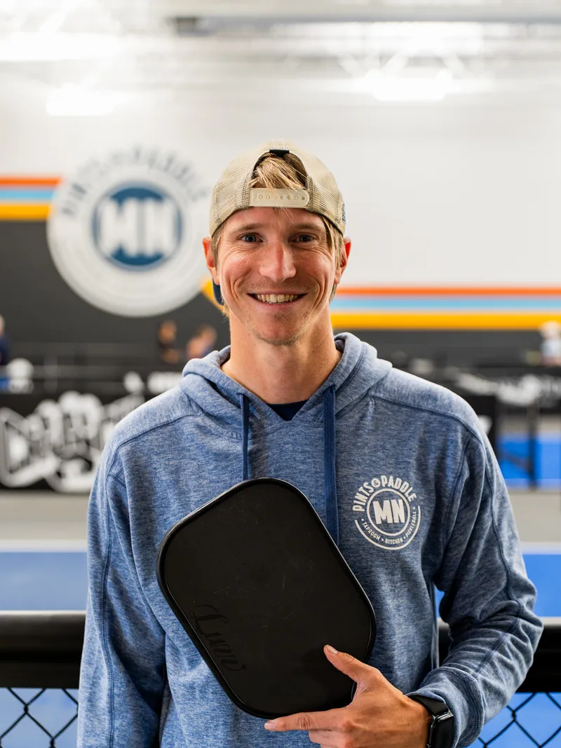 Matt Haugdahl smiling and holding a paddle on the courts at Pints & Paddle