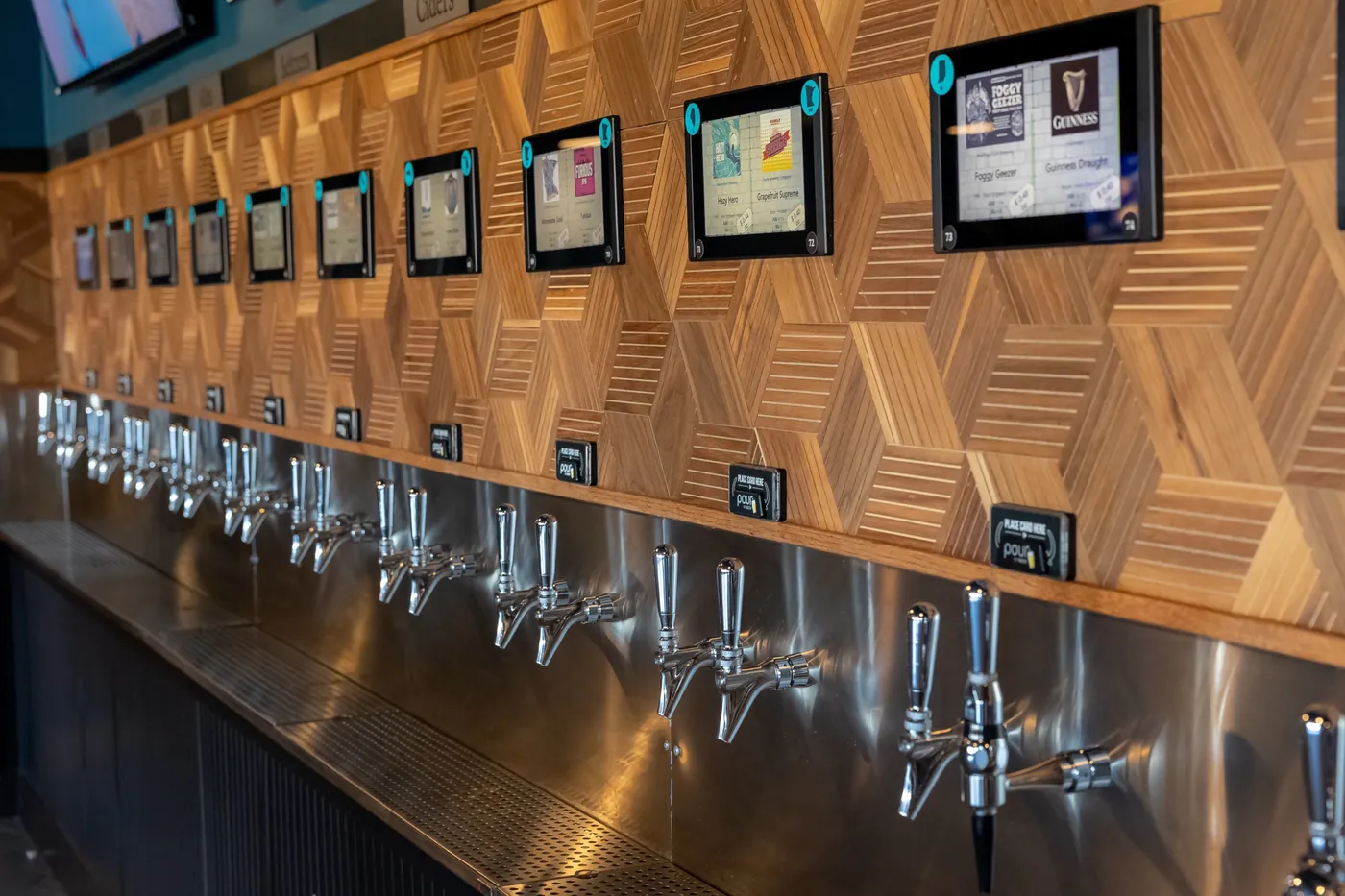 Looking down the mezzanine tap wall: a label screen above every stainless handle