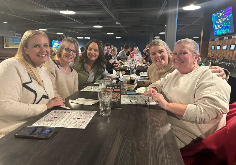 Five friends at a table on the mezzanine holding up bingo cards during a music bingo night