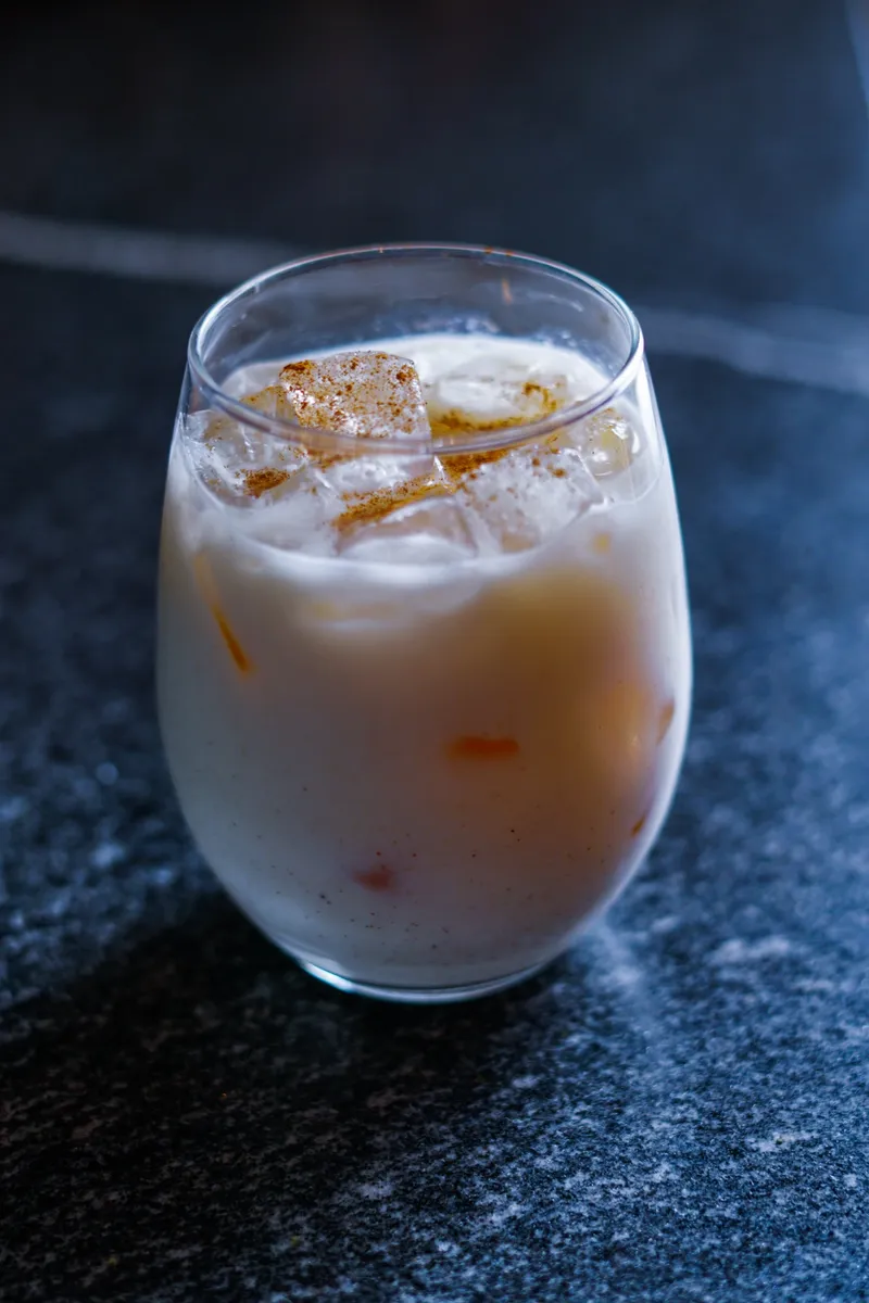 A creamy horchata colada mocktail over ice with a dusting of cinnamon in a stemless glass on a dark stone counter