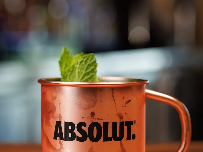 A Moscow mule in a copper mug with a mint sprig, back-bar bottles blurred behind