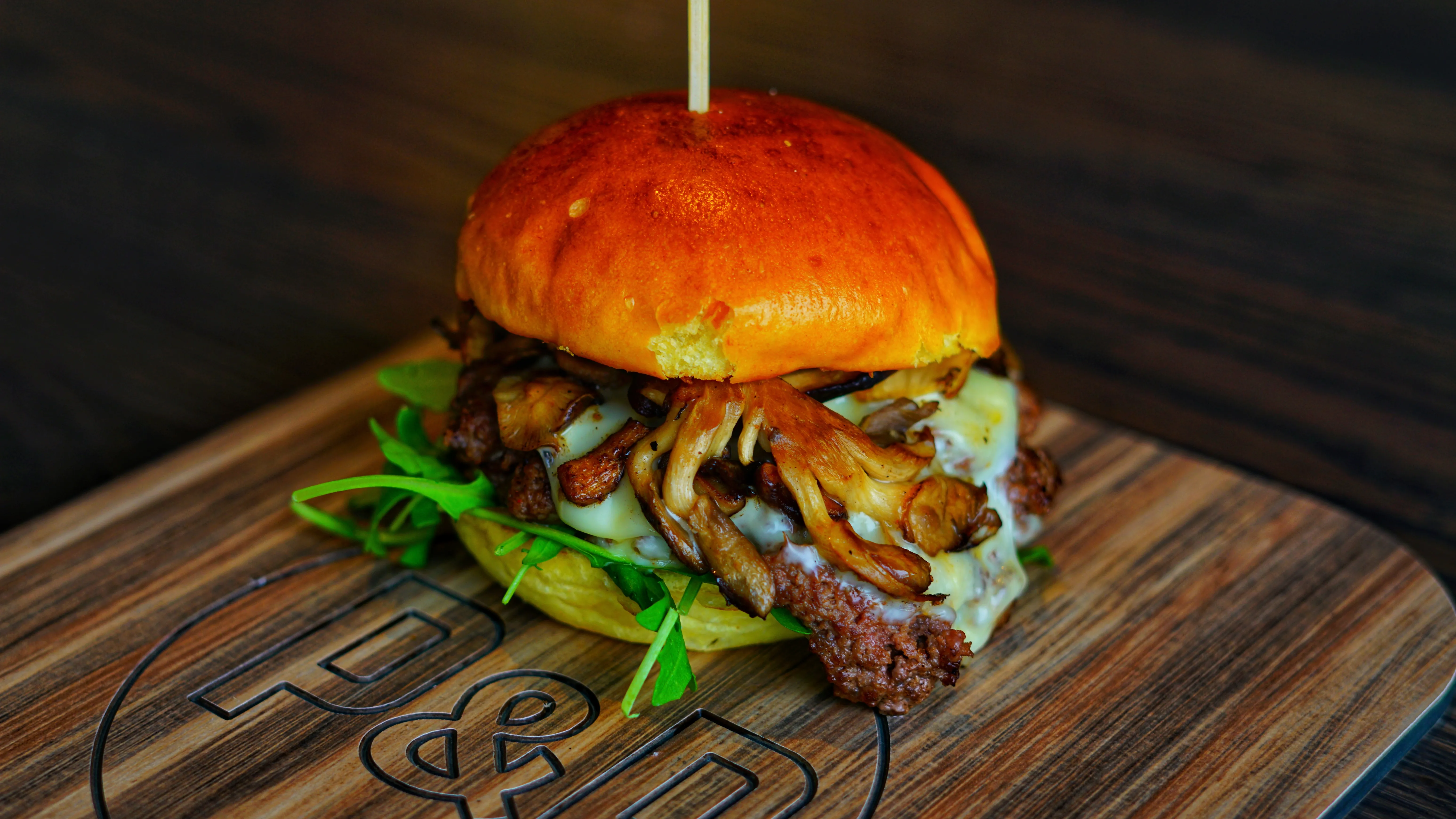 Wild Mushroom Burger topped with browned mushrooms, melted cheese and greens on a branded wooden board