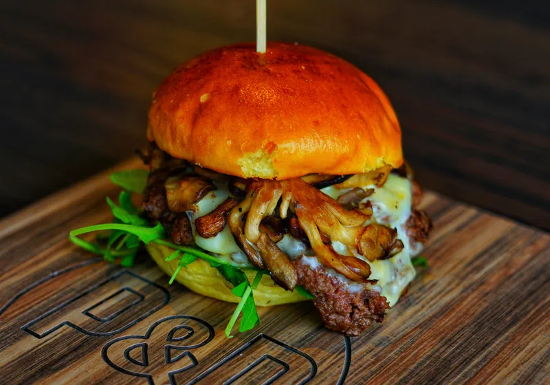 Wild Mushroom Burger topped with browned mushrooms, melted cheese and greens on a branded wooden board