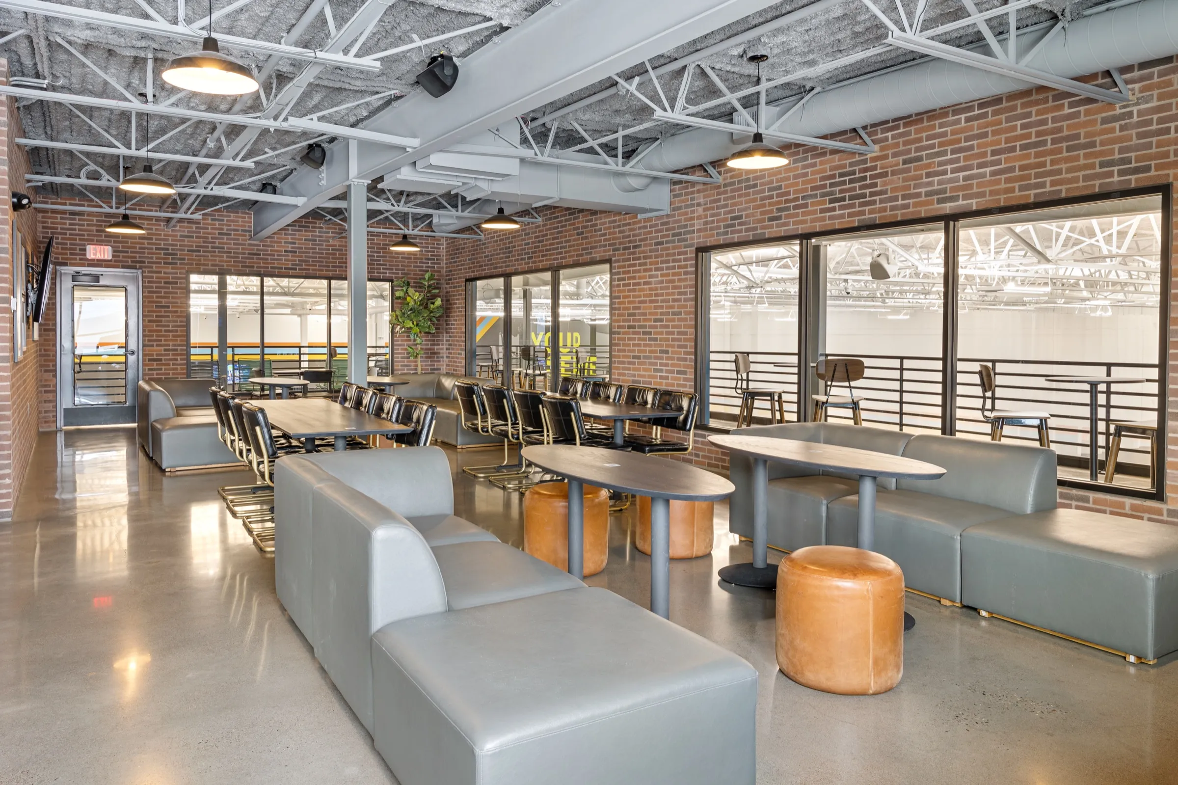 The north mezzanine lounge with grey sofas, cognac ottomans and a long table under pendant lights