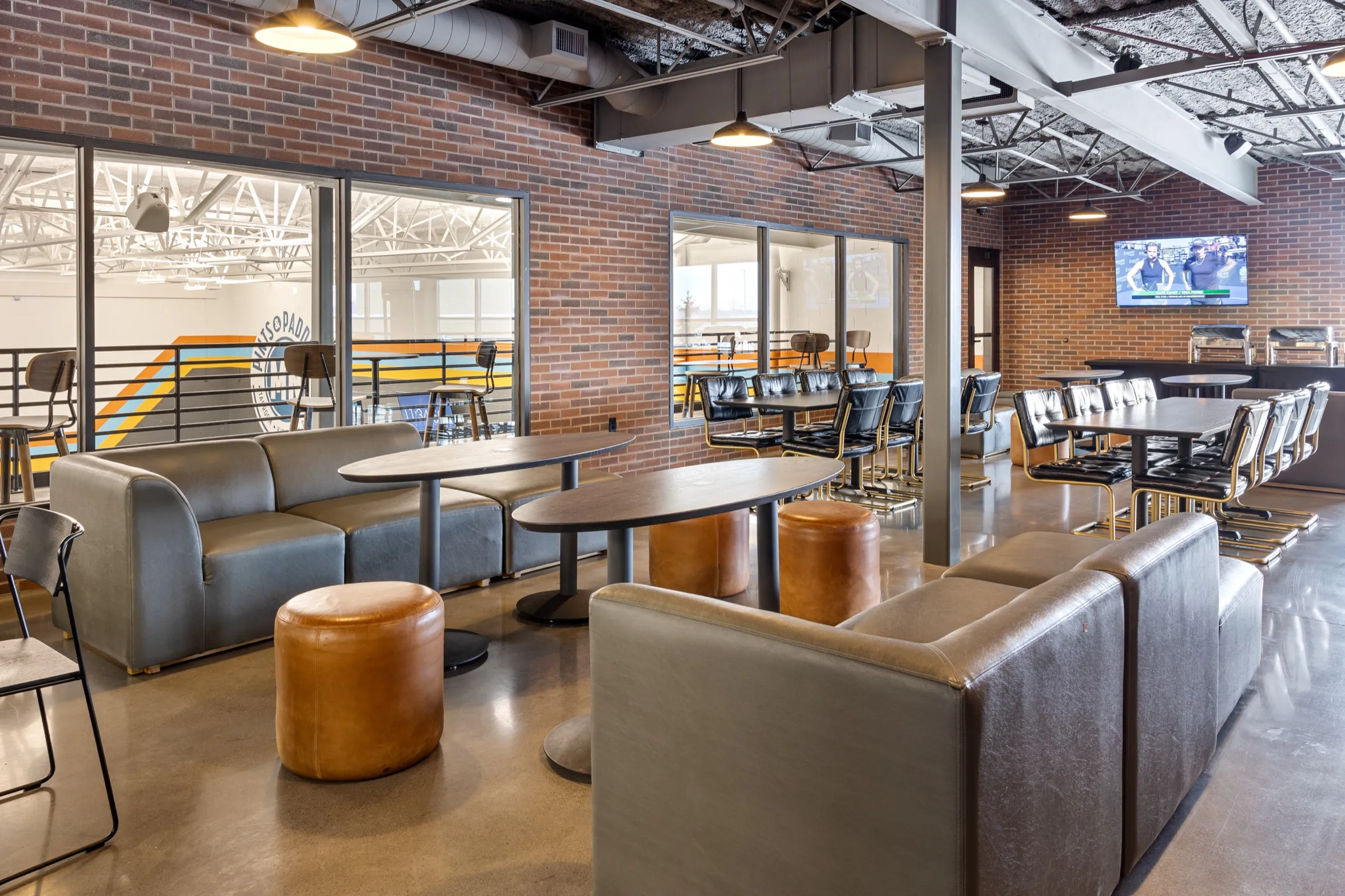 North mezzanine lounge looking toward the windows over the courts, with the Pints & Paddle logo mural visible through the glass